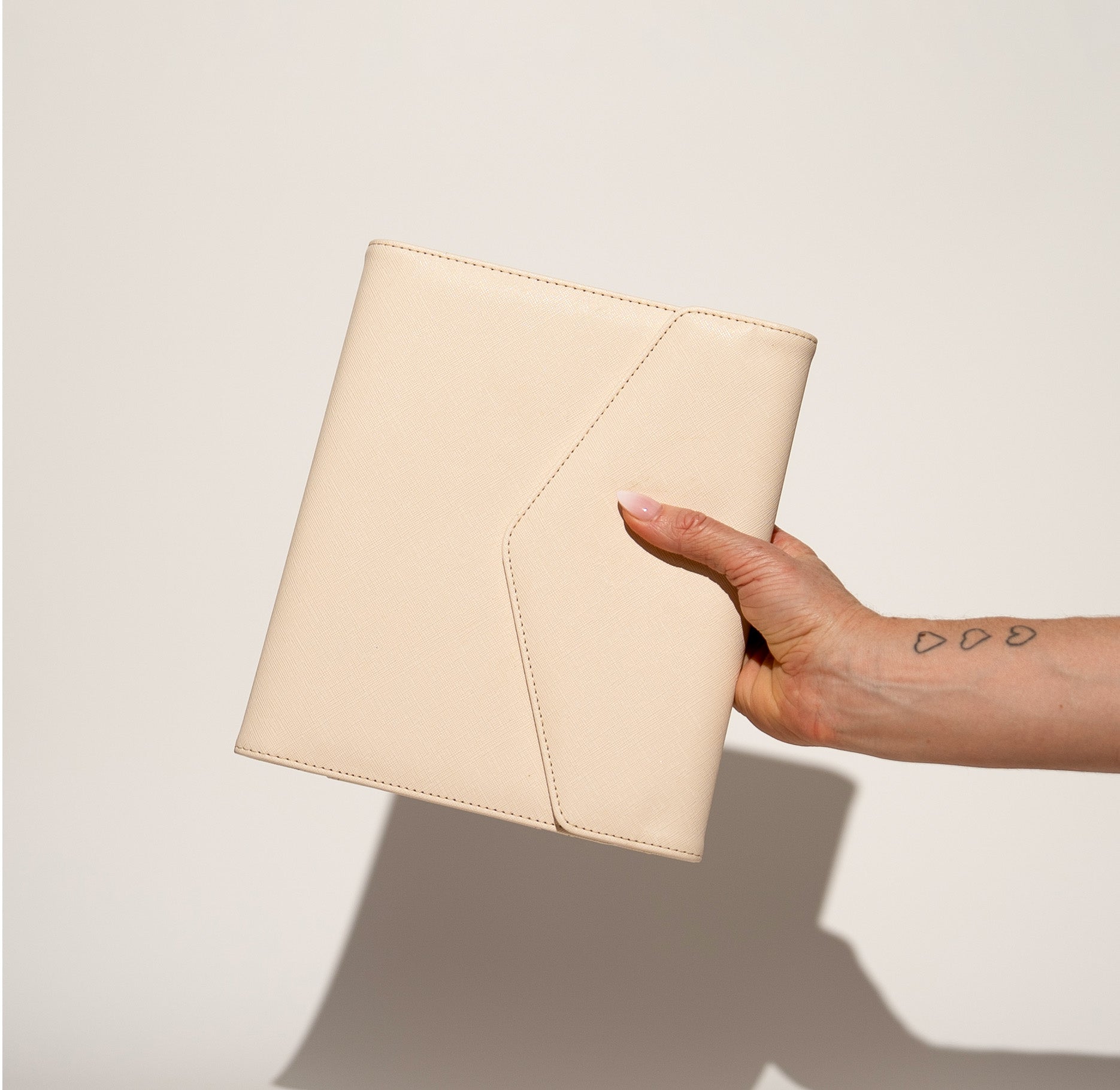 A hand holding the WTF Journal in Bone, closed, showing the envelope-fold front flap
